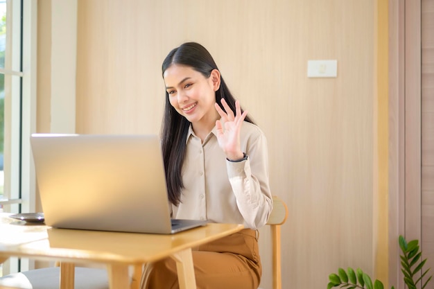 Una mujer de negocios sonriente con auriculares viendo un seminario web en una laptop y haciendo una videollamada en el lugar de trabajo