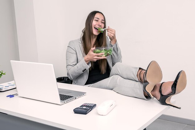 Foto mujer de negocios sonriente comiendo ensalada en el escritorio de la oficina