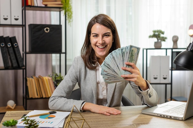 Una mujer de negocios sonriente contando dinero en efectivo chequeando sueldo disfrutando de la riqueza en la mesa de la oficina de casa