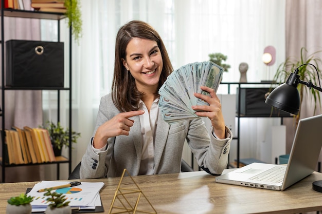 Una mujer de negocios sonriente contando dinero en efectivo chequeando sueldo disfrutando de la riqueza en la mesa de la oficina de casa