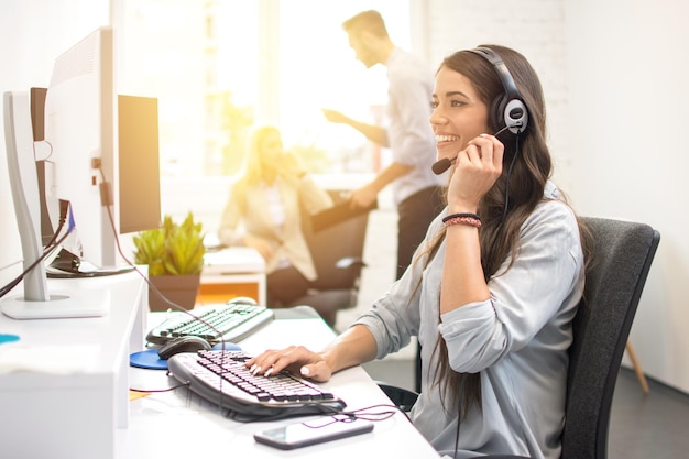 Mujer de negocios sonriente o operador de línea de ayuda con auriculares usando computadora en la oficina