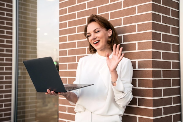 Mujer de negocios sonriente que usa una computadora portátil que agita la comunicación manual en línea, tiene una videollamada