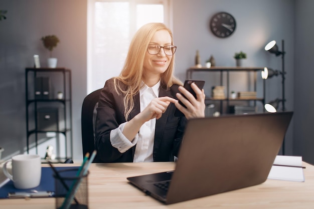 Mujer de negocios sonriente sentada en la oficina con teléfono inteligente