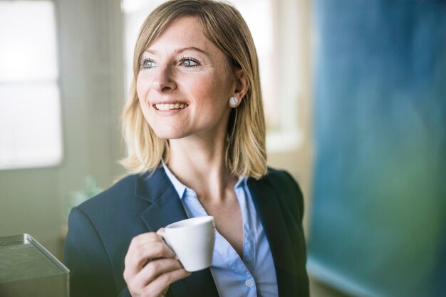 Mujer de negocios sonriente sosteniendo una taza de café en la oficina