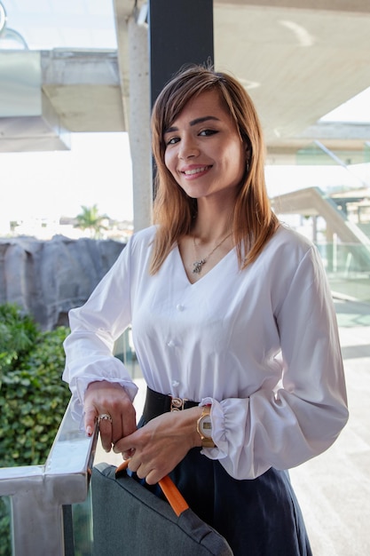 Una mujer de negocios sonriente sostiene la funda de su computadora portátil en el edificio comercial