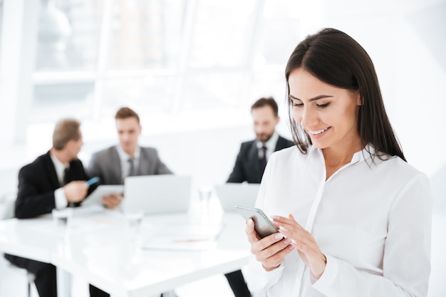 Mujer de negocios sonriente con teléfono celular con colegas en la oficina