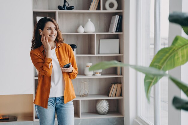 Mujer de negocios sonriente usa aplicaciones modernas de auriculares inalámbricos en el teléfono contestando llamadas chateando en casa