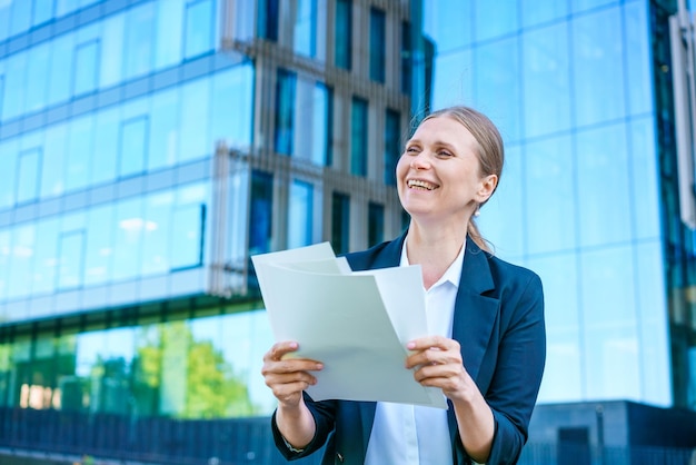 Mujer de negocios sosteniendo papeles en sus manos levantada feliz sonriendo