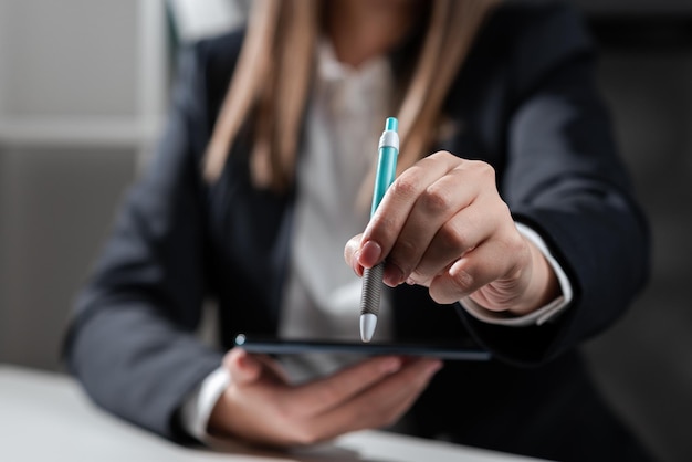 Mujer de negocios sosteniendo tableta en una mano y señalando con bolígrafo en un mensaje importante mujer sentada en la oficina con teléfono móvil en la mano presentando información