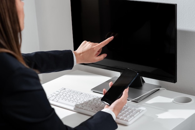 Mujer de negocios sosteniendo un teléfono móvil y señalando en la pantalla de la computadora con un mensaje importante mujer