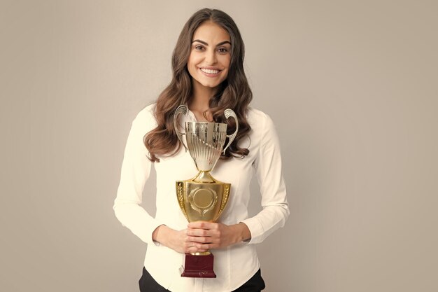 Mujer de negocios sosteniendo un trofeo Éxito del ganador del concepto de mujer de negocios Mujer sonriente con trofeo aislado sobre fondo gris Empleado exitoso sostiene la copa del ganador Ceremonia de premiación para el ganador Mejor