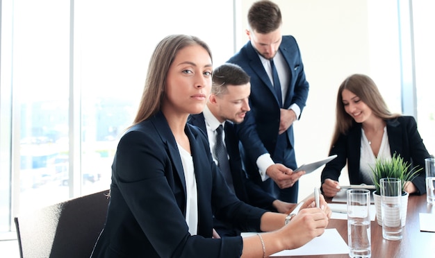 Mujer de negocios con su personal, grupo de personas en segundo plano en la oficina moderna y luminosa en el interior