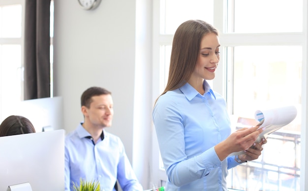 Mujer de negocios con su personal, grupo de personas en segundo plano en la oficina moderna y luminosa en el interior.