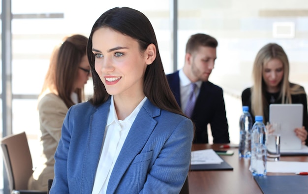 Foto mujer de negocios con su personal, grupo de personas en segundo plano en la oficina moderna y luminosa en el interior.