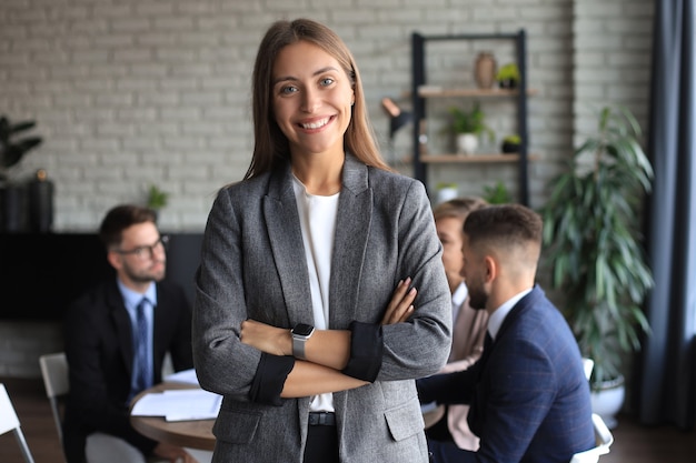 Mujer de negocios con su personal, grupo de personas en segundo plano en la oficina moderna y luminosa en el interior.