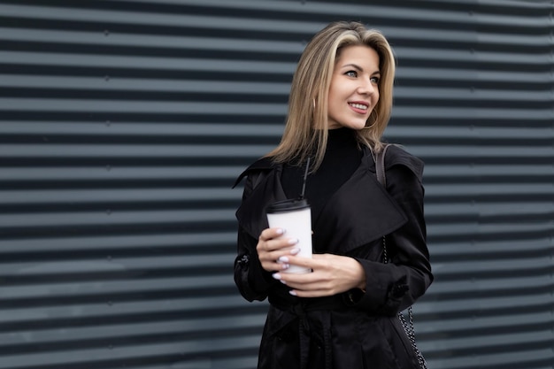 Mujer de negocios con una taza de café en las manos y una sonrisa en un fondo de grafito gris