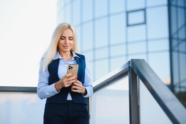 Mujer de negocios con teléfono cerca de la oficina Retrato de una hermosa mujer sonriente en ropa de oficina de moda hablando por teléfono mientras está de pie al aire libre Comunicación telefónica Imagen de alta calidad