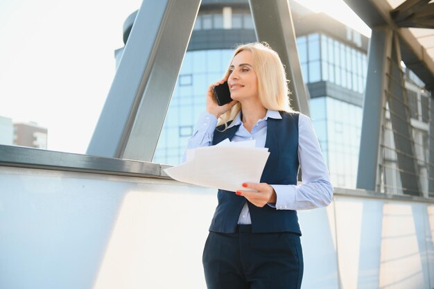 Mujer de negocios con teléfono cerca de la oficina Retrato de una hermosa mujer sonriente en ropa de oficina de moda hablando por teléfono mientras está de pie al aire libre Comunicación telefónica Imagen de alta calidad