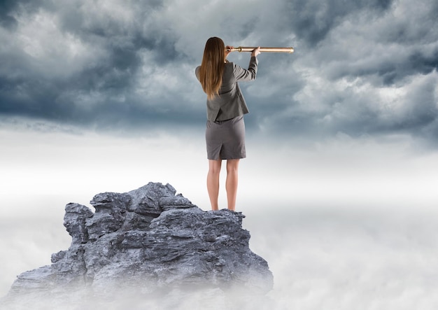 Mujer de negocios con telescopio en el pico de la montaña contra las nubes de tormenta