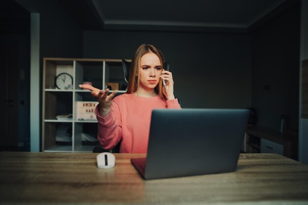 La mujer de negocios trabaja en casa en una mesa en una computadora portátil y llama a un teléfono inteligente