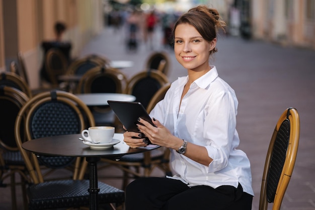 Mujer de negocios trabajando al aire libre en la terraza de un café usando una tableta independiente