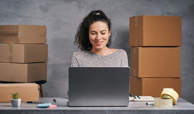 Mujer de negocios trabajando desde casa con laptop y preparando cajas con productos para enviar