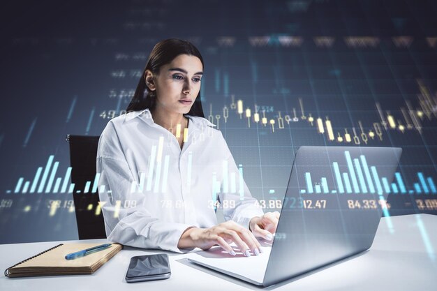 Mujer de negocios trabajando en una computadora portátil con gráficos financieros y gráficos superpuestos en la oficina