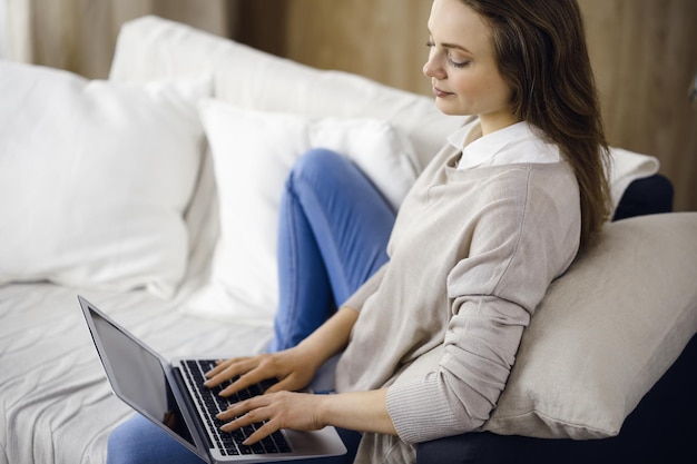 Mujer de negocios trabajando en una computadora portátil sentada en el interior durante la cuarentena de Covid-19 en una acogedora sala de estar.