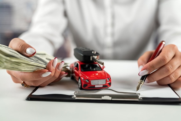 Mujer de negocios trabajando en documentos de seguro con un automóvil pequeño sobre la mesa Seguro de vida y automóvil Dólares sobre la mesa