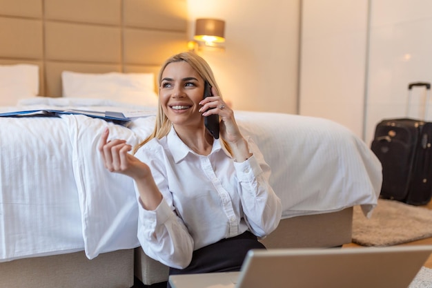 Foto mujer de negocios trabajando desde una habitación de hotel hermosa mujer joven hablando por teléfono móvil inteligente sentada en el suelo divirtiéndose en un viaje de negocios