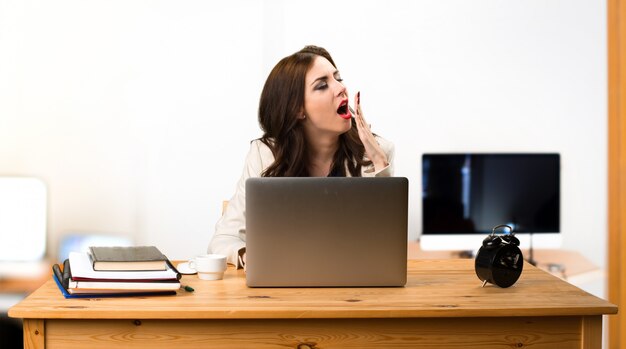 Mujer de negocios trabajando con su computadora portátil y bostezando en la oficina