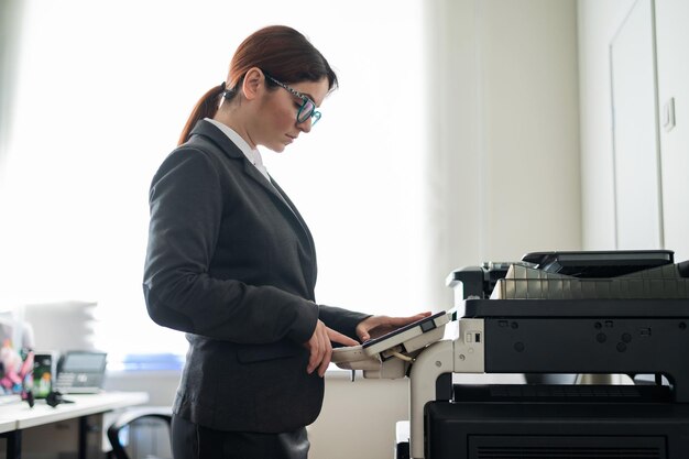 Foto mujer de negocios con traje y anteojos hace copias de documentos en una fotocopiadora gerente de oficina femenina está haciendo papeleo secretaria hace fotocopias