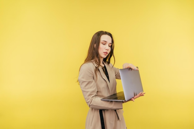 Una mujer de negocios con traje beige abre una laptop para trabajar con una cara seria en un fondo amarillo