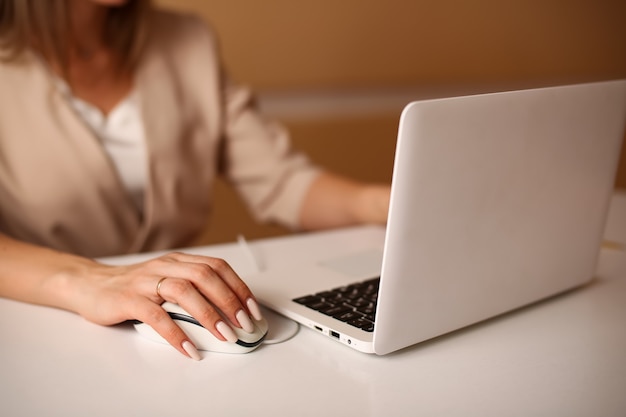 Mujer de negocios en traje formal beige trabaja en la mano de la computadora y el primer plano del ratón de la computadora en una imagen borrosa de una mujer