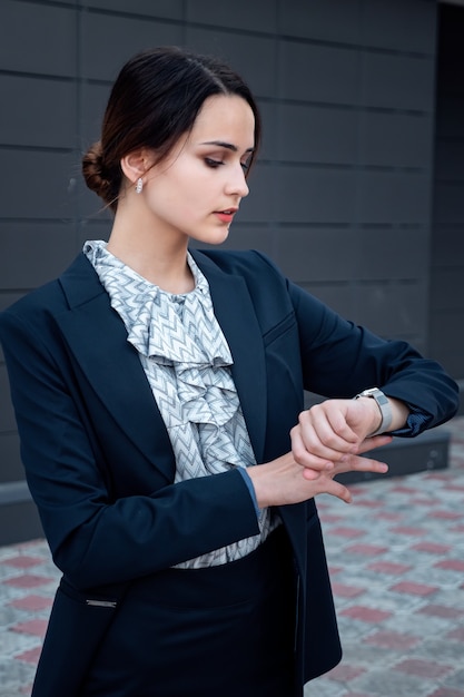 Mujer de negocios en traje mira el reloj, al aire libre.