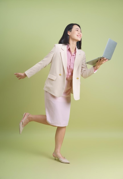 Mujer de negocios en traje pastel alegremente sostiene la computadora portátil mientras se equilibra en una pierna en brillante