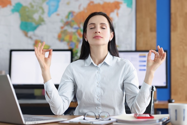 Mujer de negocios tranquila haciendo ejercicios de yoga en el lugar de trabajo