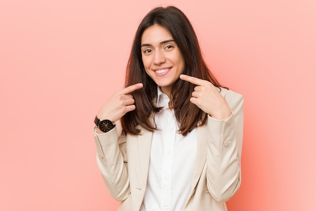 La mujer de negocios triguena joven en rosa sonríe, señalando los dedos en la boca.