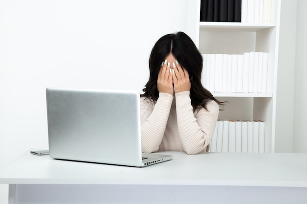 Mujer de negocios triste y cansada que trabaja en el escritorio en la computadora. Concepto de dolor de cabeza.