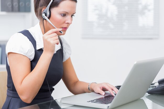 Mujer de negocios usando auriculares y usando la computadora portátil en la oficina