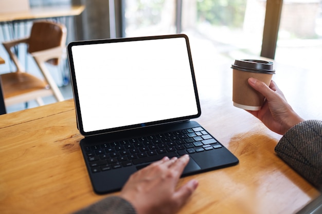 De una mujer de negocios usando y escribiendo en el teclado de la tableta con una pantalla de escritorio en blanco como una computadora mientras toma café en la oficina