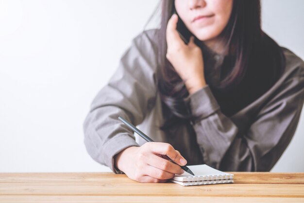 Mujer de negocios usando el teléfono y escribir cuaderno