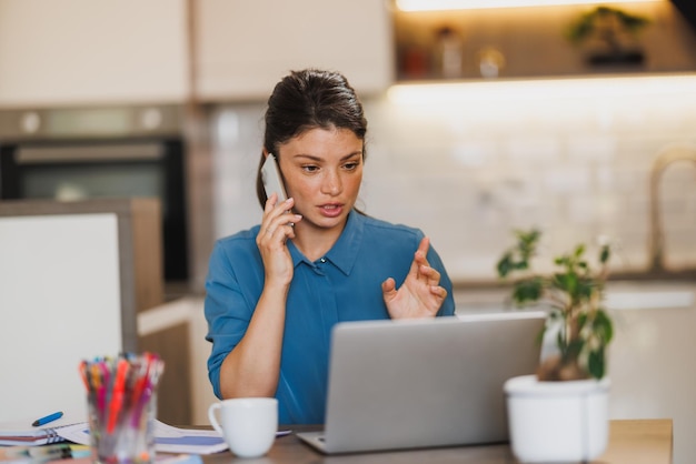 Foto mujer de negocios usando un teléfono inteligente mientras trabaja en una computadora portátil desde su oficina en casa.