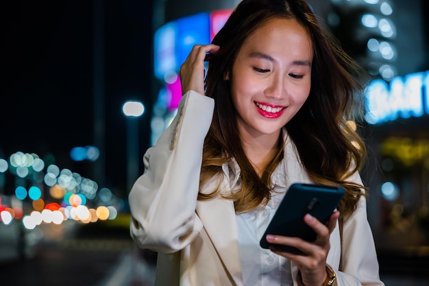 Mujer de negocios usando teléfono móvil caminando por la calle de la ciudad de noche