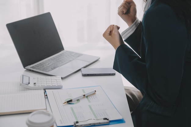 Mujer de negocios usando teléfono móvil mientras trabaja en una computadora portátil navegando por Internet buscando datos comerciales en una oficina moderna Mujer de negocio asiática en línea trabajando en la computadora en el lugar de trabajo