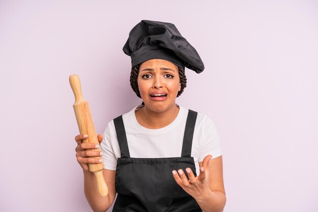 Mujer negra afro que parece desesperada, frustrada y estresada. chef con un rodillo