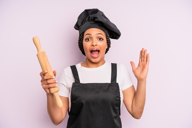 Mujer negra afro que se siente feliz y asombrada por algo increíble chef con un rodillo