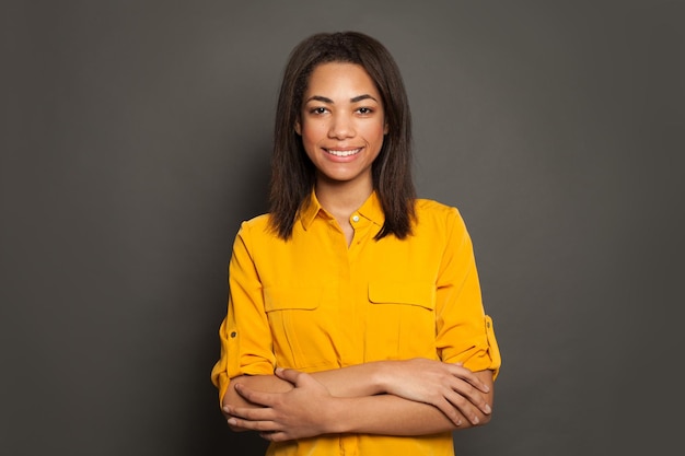 Mujer negra afroamericana sonriente con los brazos cruzados sobre un fondo gris