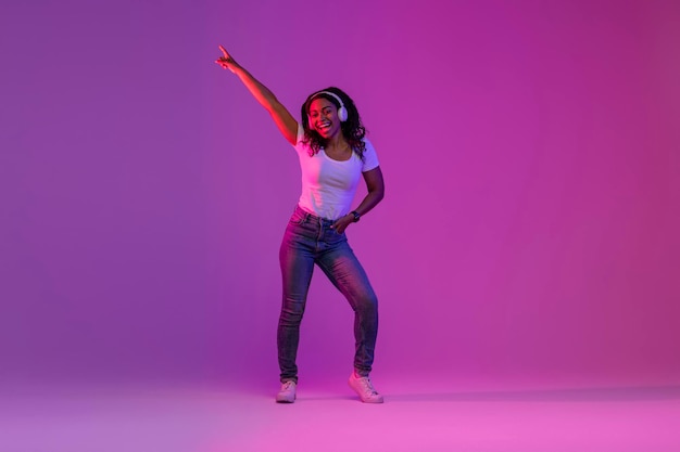 Foto mujer negra alegre con auriculares inalámbricos divirtiéndose en luz de neón