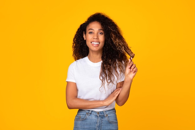 Mujer negra alegre con cabello rizado posando contra un fondo amarillo